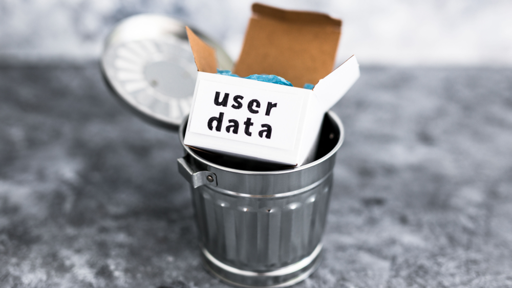 Brun pappeske merket "user data" kastet i en søppelbøtte av metall på grå bakgrunn.