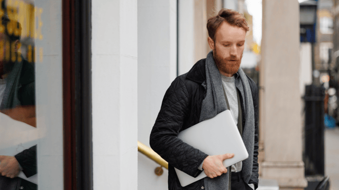 Ansatt på vei ut av kontorbygg med laptop under armen, symbol på avslutning av arbeidsforhold