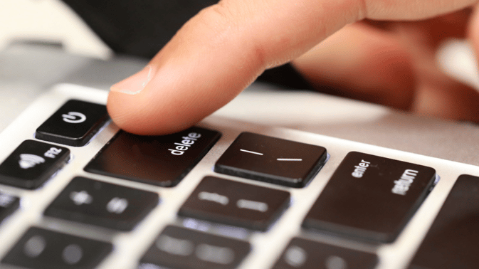 En finger trykker på "delete"-tasten på et tastatur, symboliserer sletting av data.